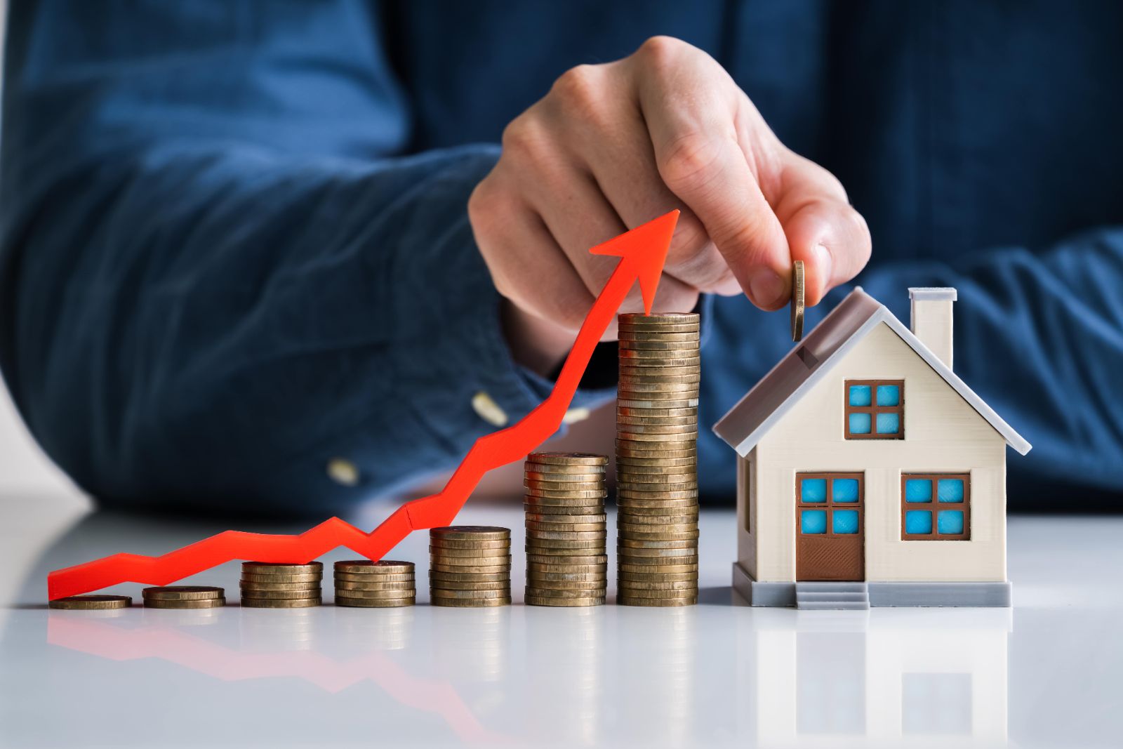 Stacks of coins and a model house with a rising arrow